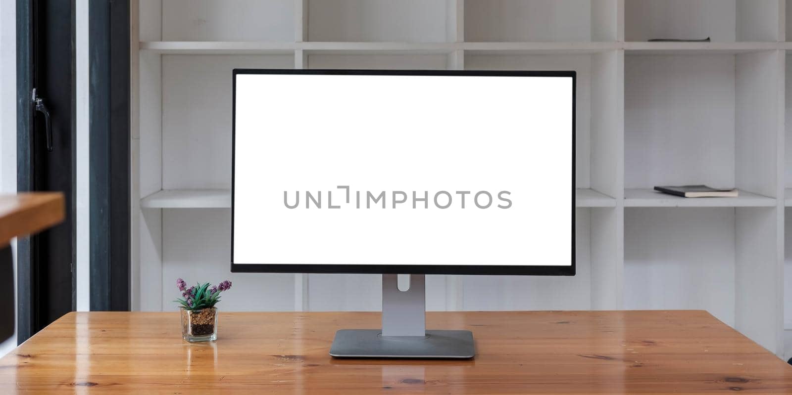 Close up view of simple workspace with open blank screen laptop, frame and notebook on white table with blurred office room background by wichayada