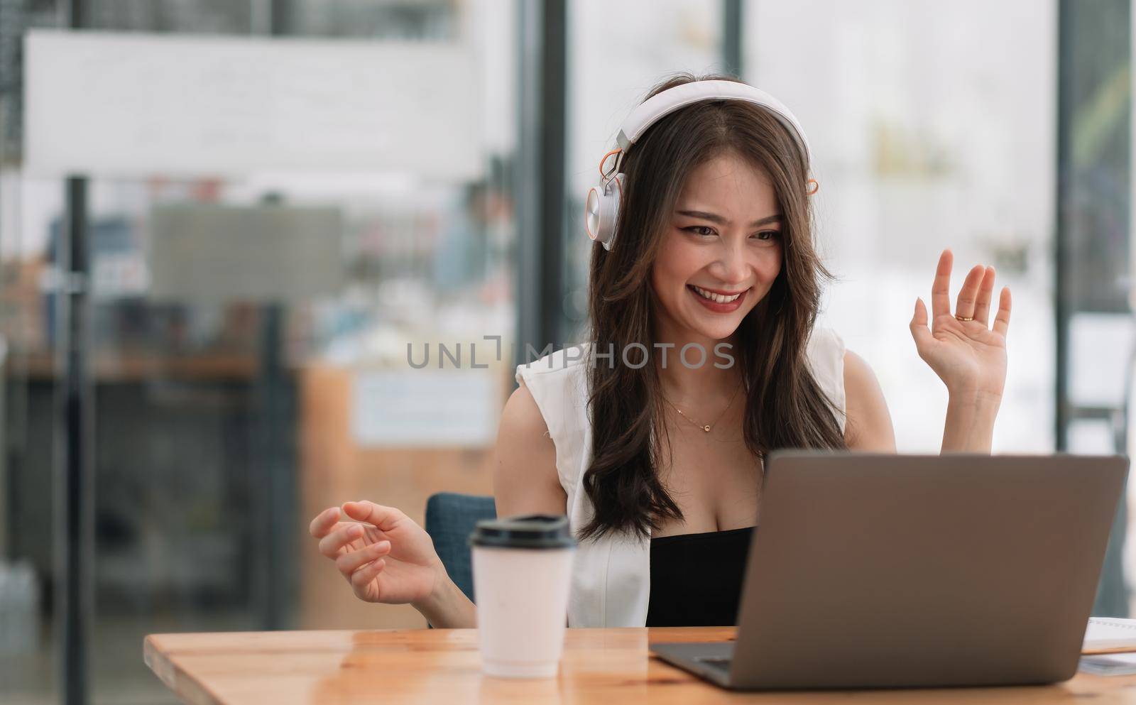 Smiling girl student wear wireless headphone study online with teacher, happy young asian woman learn language listen lecture watch webinar write notes look at laptop sit in cafe, distant education