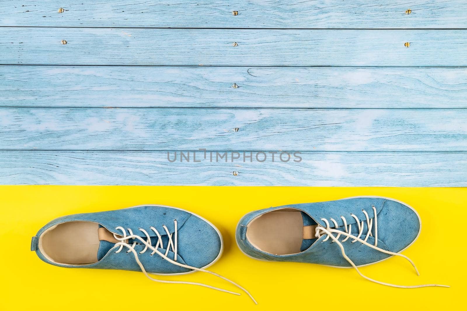 The blue shoes stand on an isolated mixed blue and yellow background.