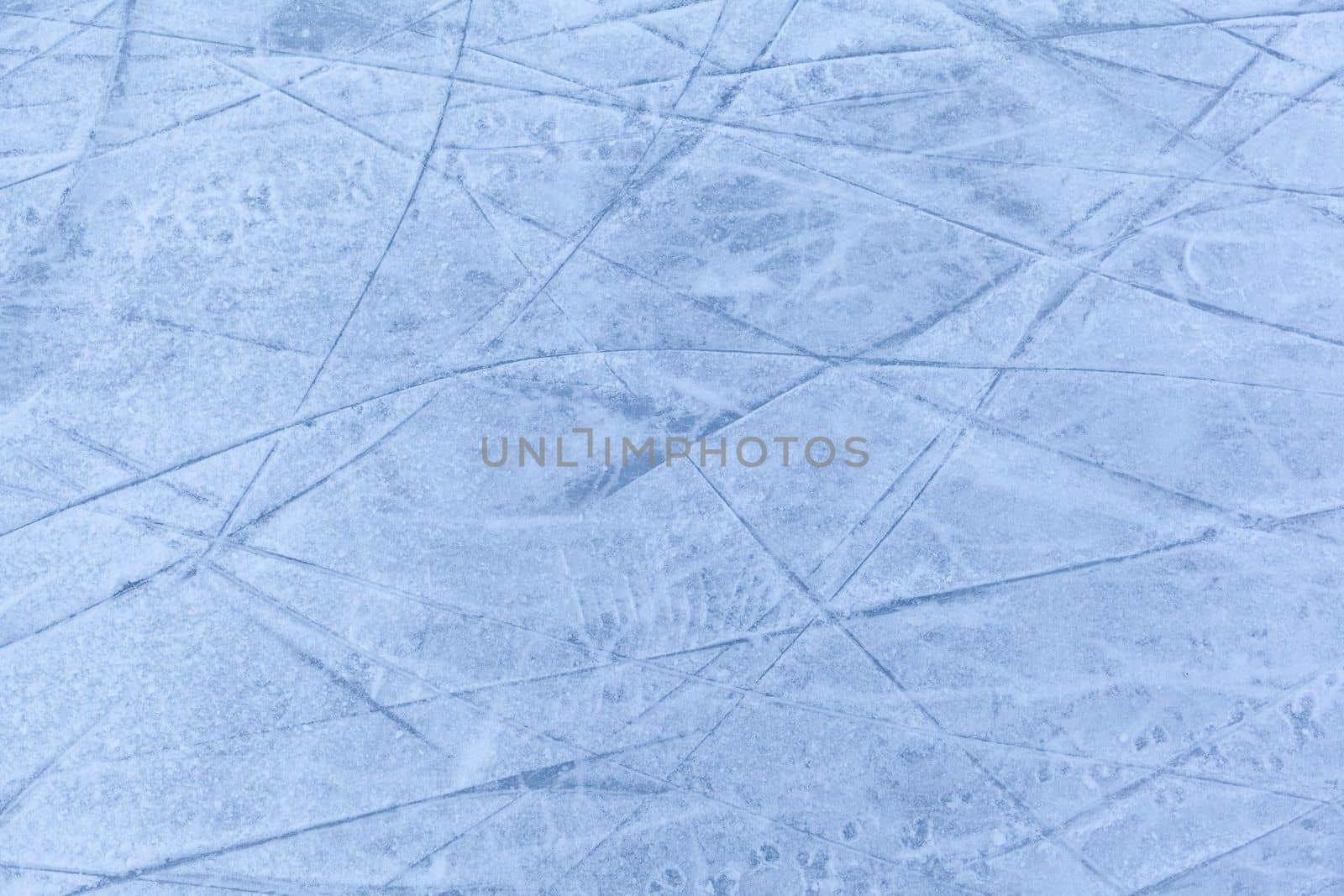 Empty ice rink with skate marks after the session outdoor. skating ice rink texture covered with snow in daylight. Close up of blue ice rink floor, copy space