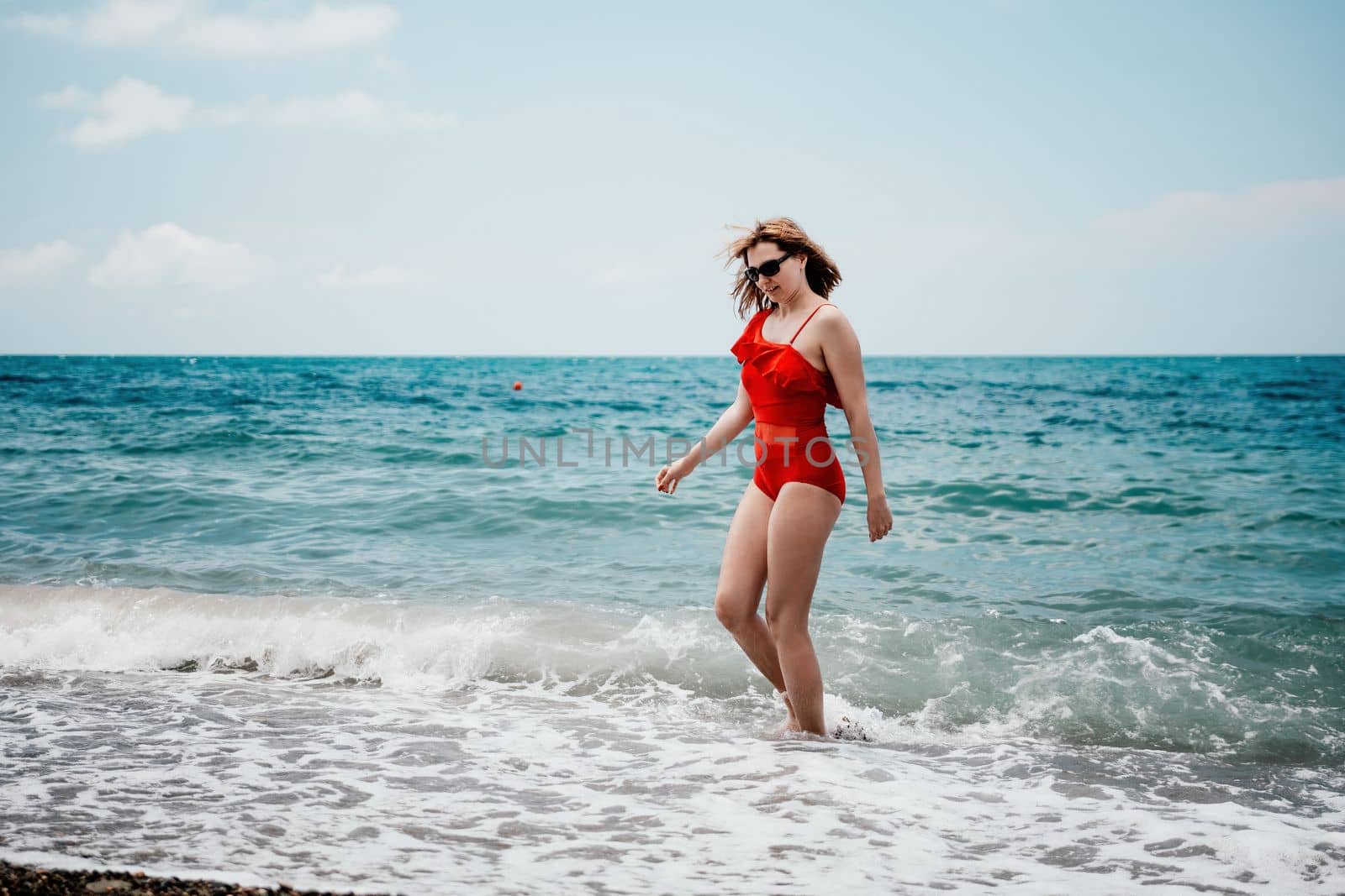 Young happy woman walks carefree on the seaside. Happy lady in red bikini. Portrait beautiful young woman relax smile around beach sea ocean in holiday vacation travel trip.