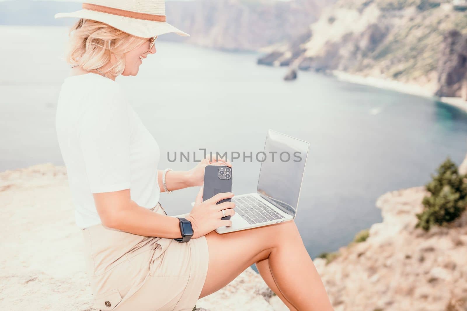 Digital nomad, Business woman working on laptop by the sea. Pretty lady typing on computer by the sea at sunset, makes a business transaction online from a distance. Freelance remote work on vacation