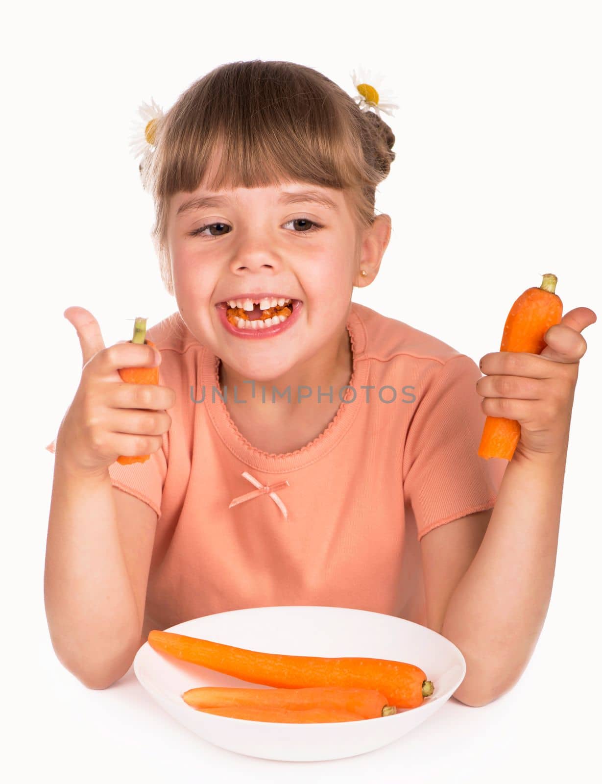 Problems of pediatric dentistry. Little girl in an orange t-shirt and flowers in her hair eats a carrot on a white background by aprilphoto