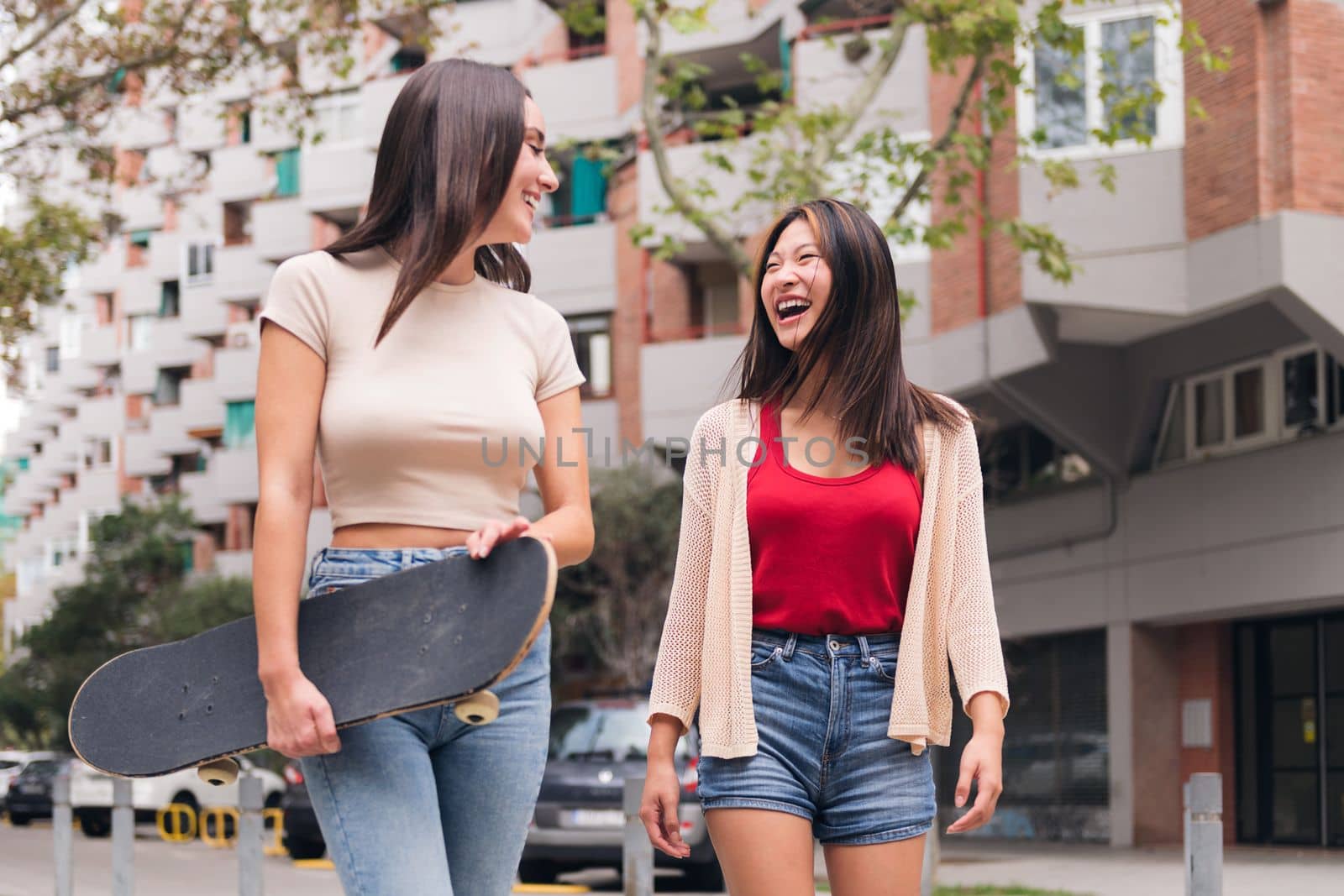 two young women friends laughing and walking happy through the city, concept of female friendship and teenager lifestyle