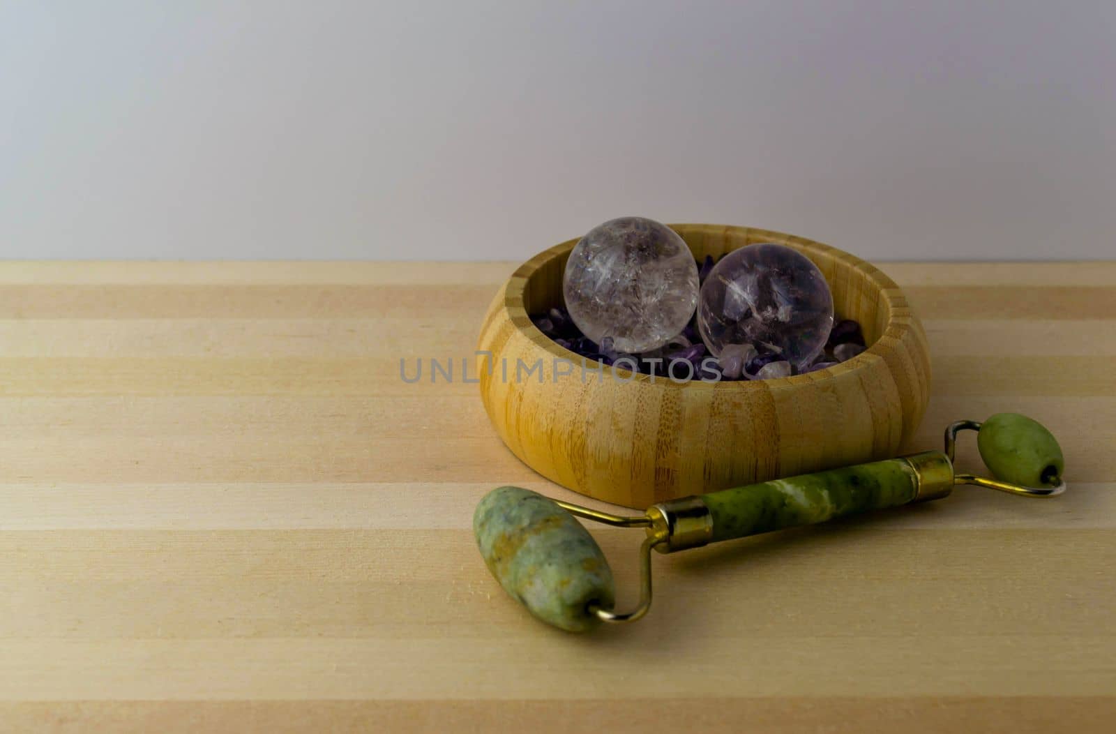 Jade roller crystal balls with amethyst stones on a wooden table.