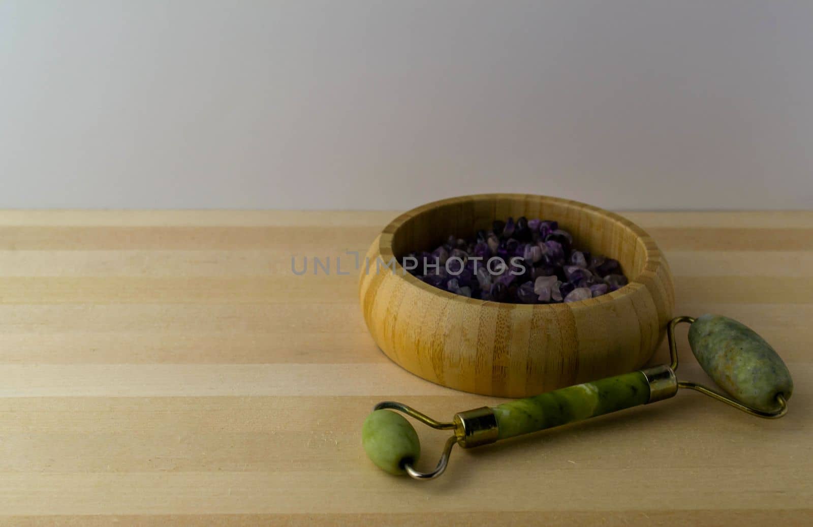 Jade roller with amethyst stones on a wooden table.