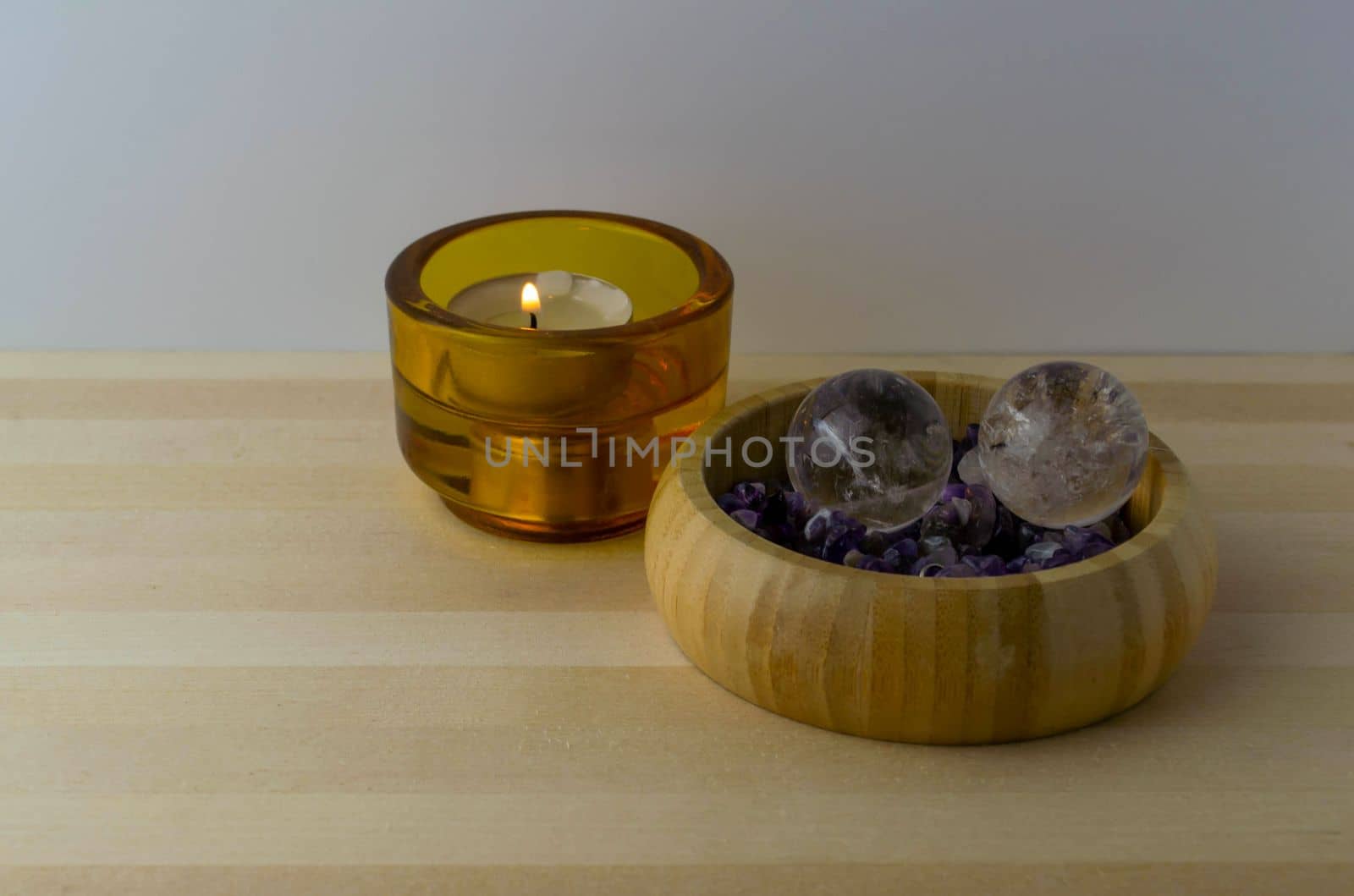 Crystal balls with amethyst stones and a burning candle on a wooden table.