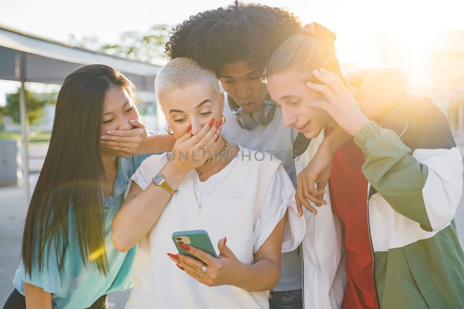 Cheerful group of friends looking smart phone surprised and excited outdoors. Smiling young people. by PaulCarr