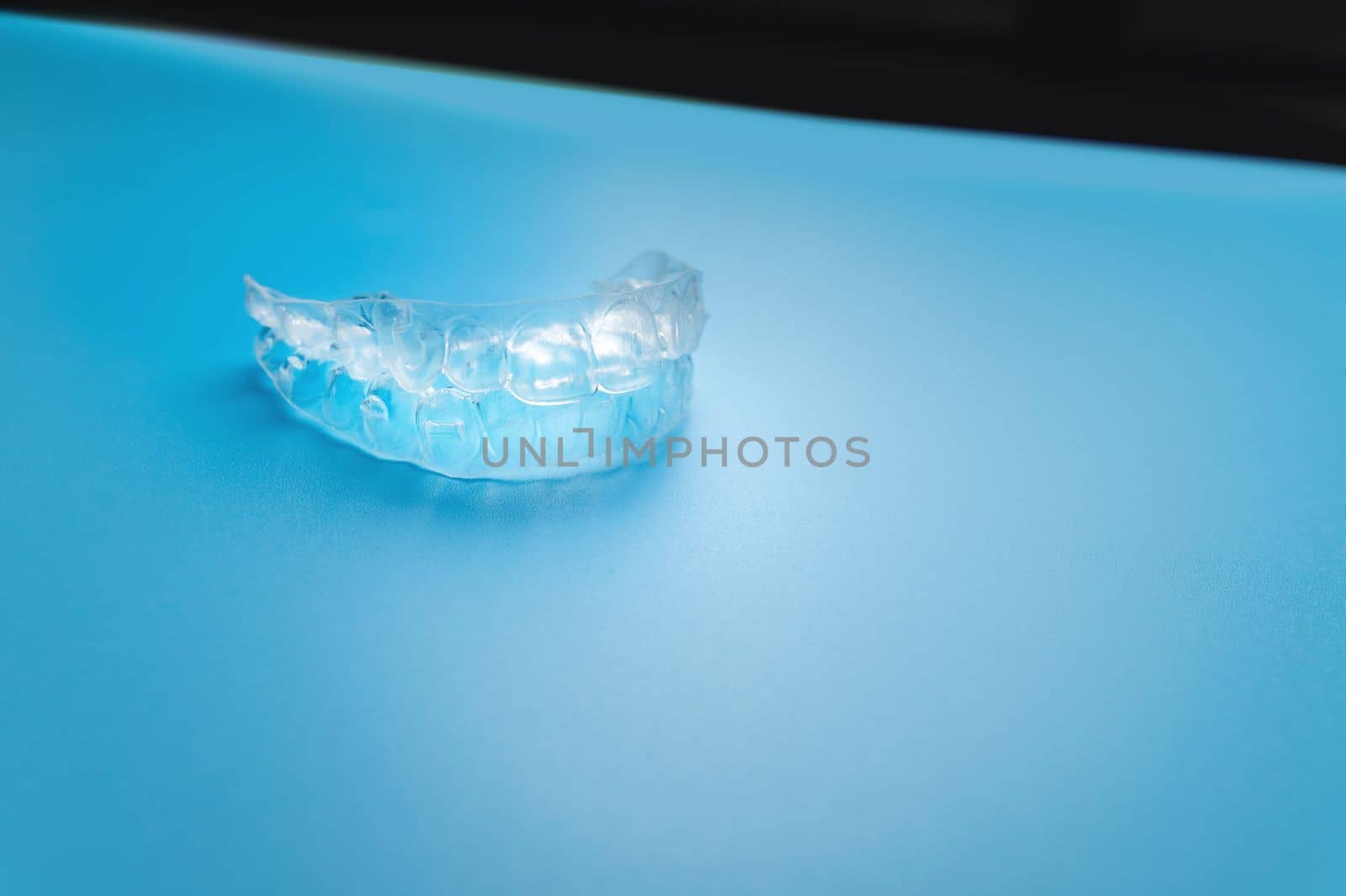 A transparent aligner lies on a bright background. No people.