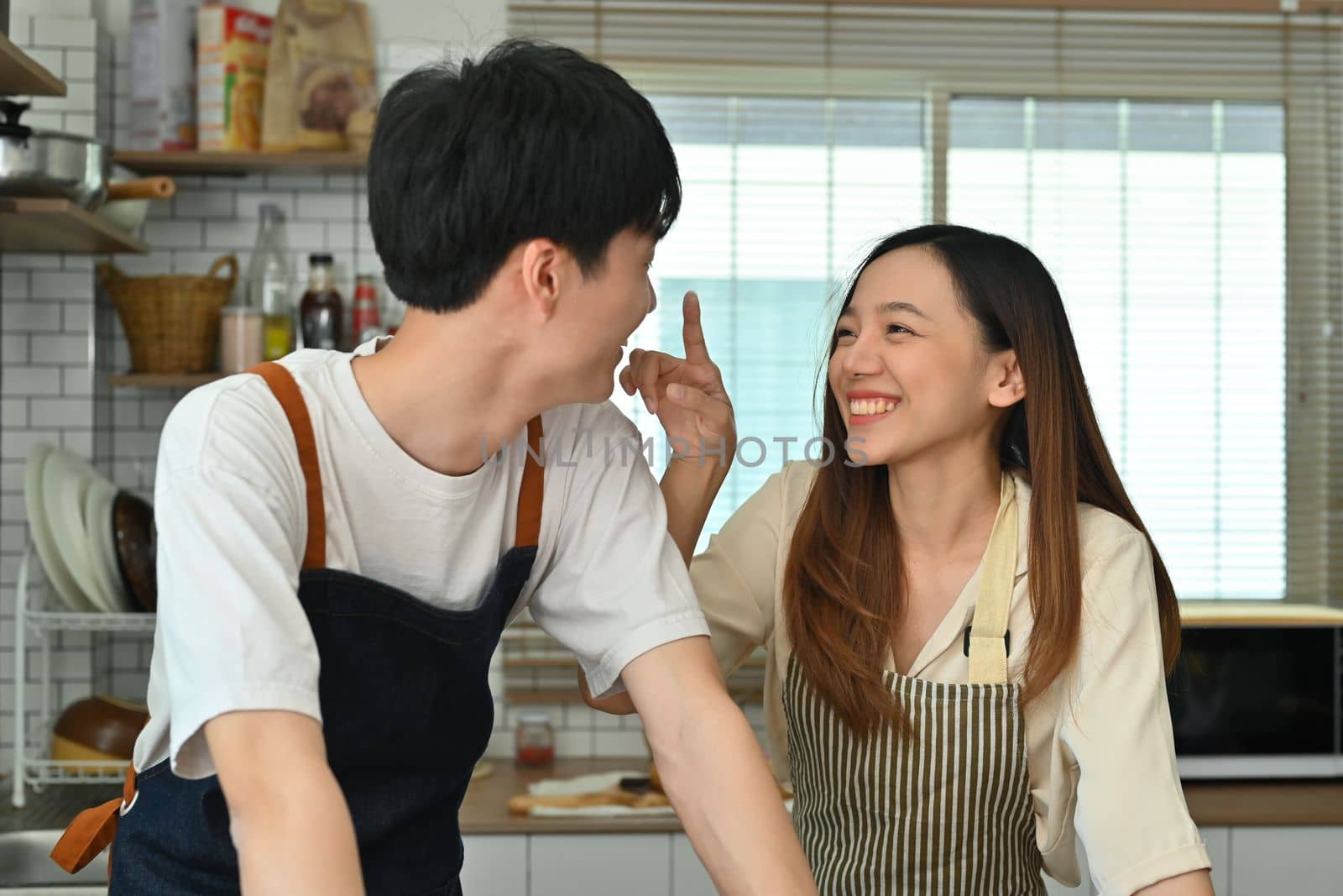 Playful young asian couple enjoying romantic family time in modern kitchen, spending leisure weekend time together at home by prathanchorruangsak