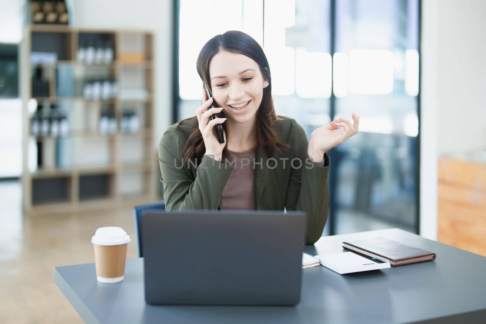 Portrait of a young Asian Woman showing a smiling face as she uses his smartphone mobile, notebook and computer laptop on her desk in the early morning hours. by Manastrong