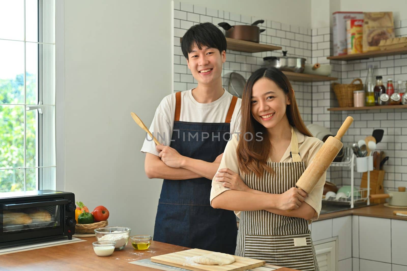 Happy loving couple with rolling pins in their hand, preparing dinner in modern kitchen,enjoying leisure time at home by prathanchorruangsak