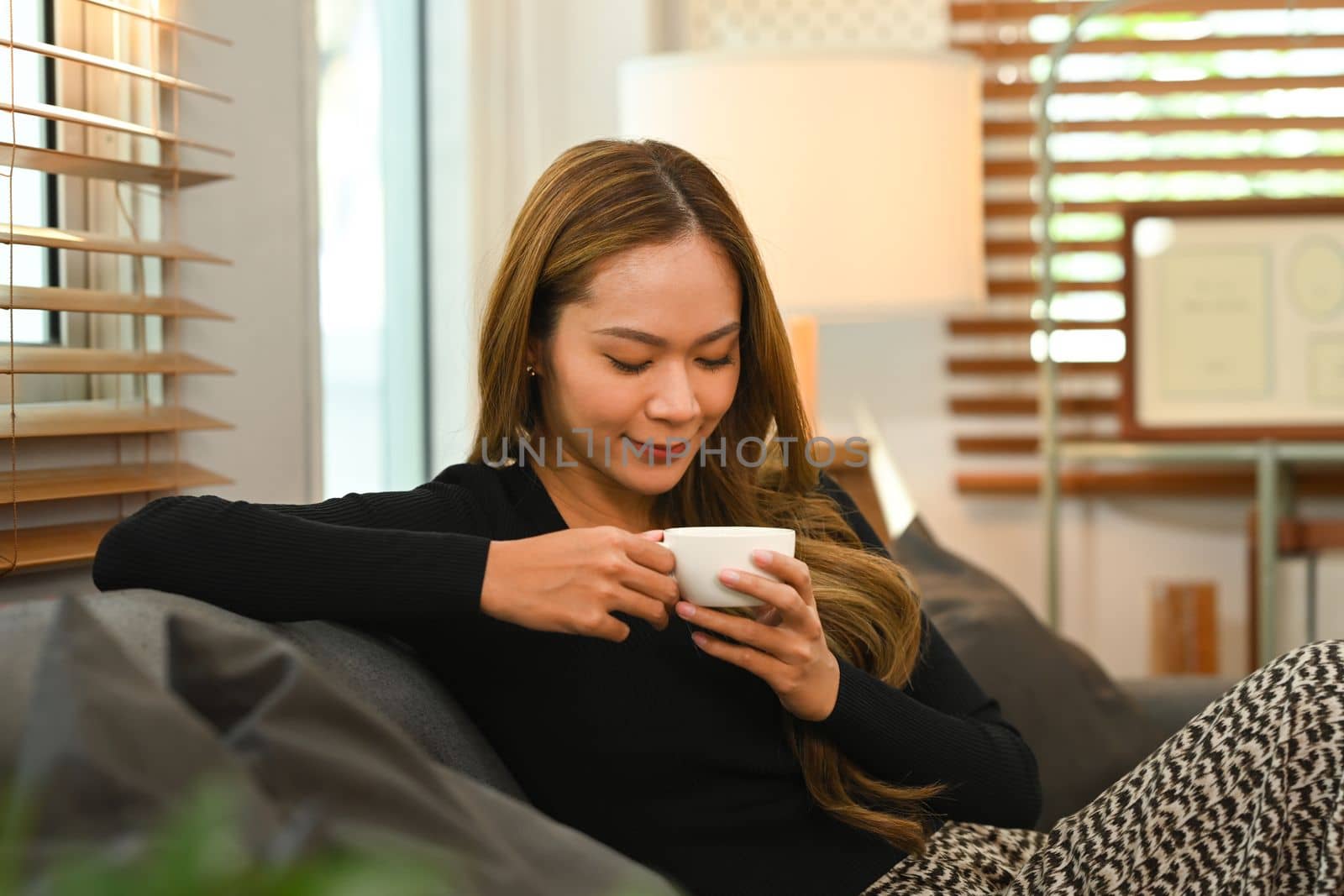 Relaxed woman in casual clothes enjoying her morning coffee on comfortable couch at home.
