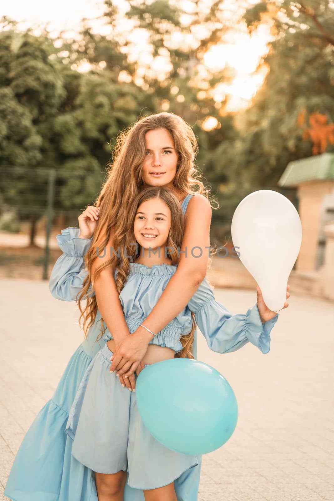 Mother daughter sunset. in blue dresses with flowing long hair a by Matiunina