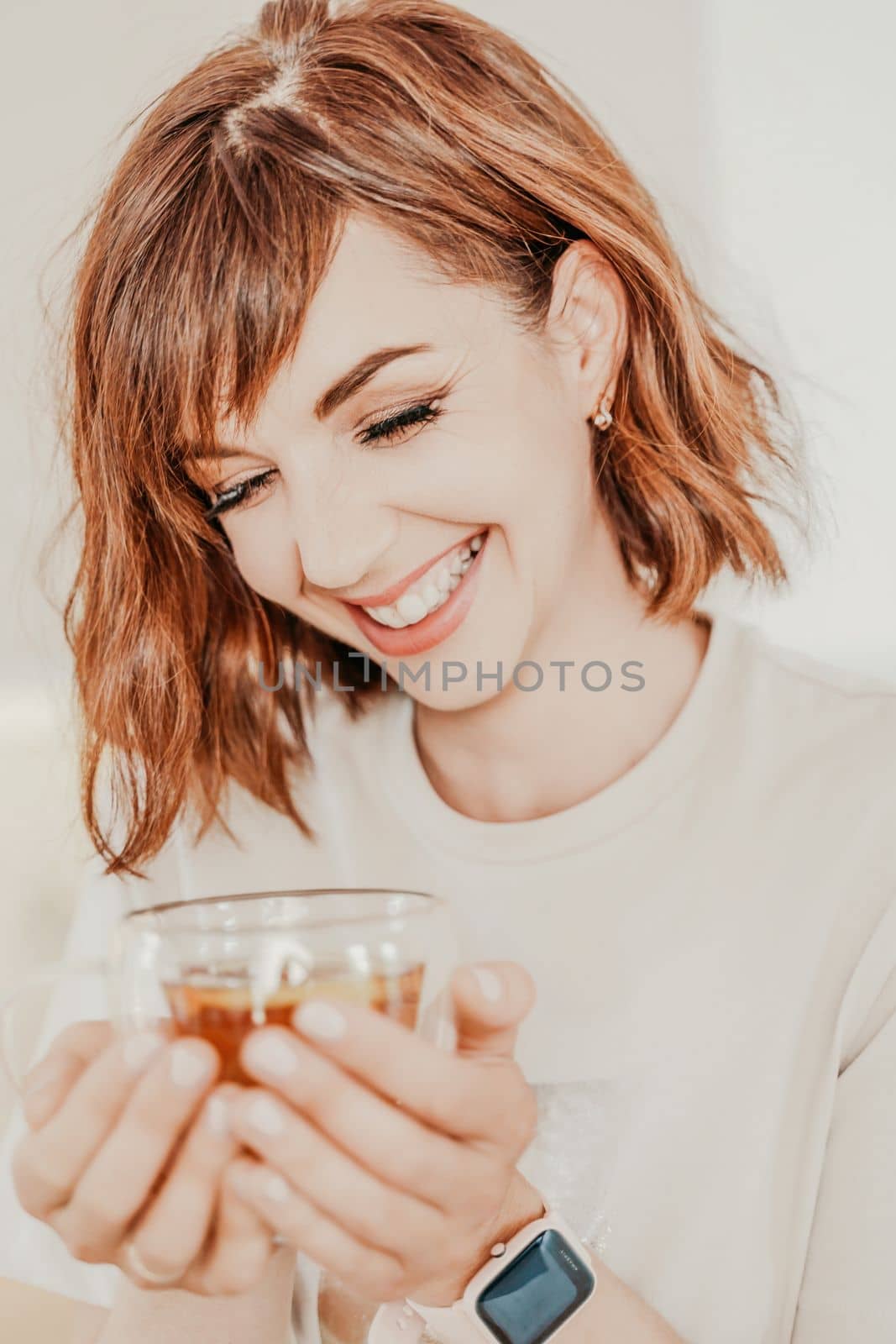 Woman drinks tea close-up. Portrait of a brunette in a white T-shirt with a transparent mug in her hands