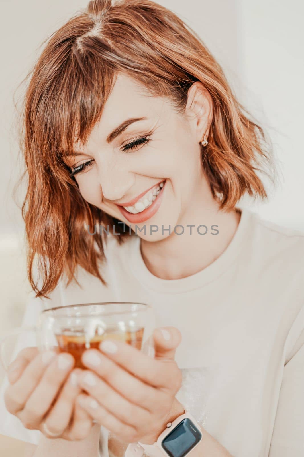 Woman drinks tea close-up. Portrait of a brunette in a white T-shirt with a transparent mug in her hands. by Matiunina