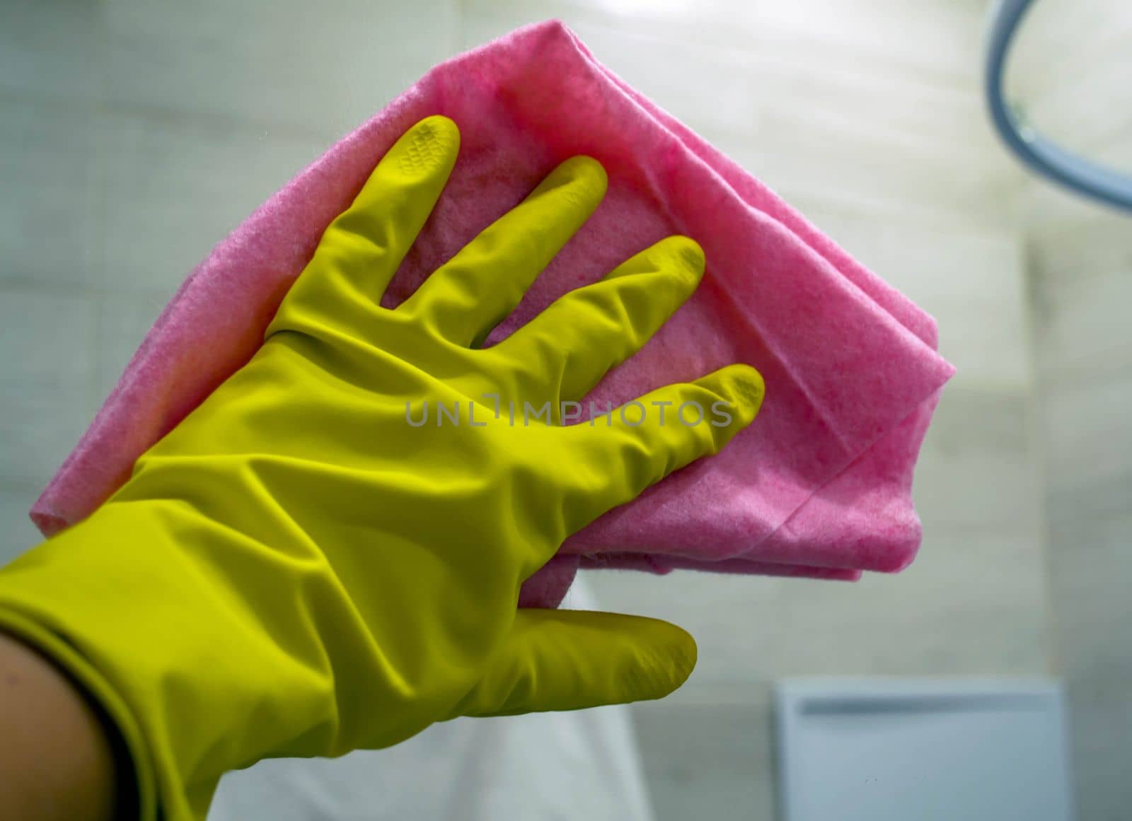 Cleaning. In the photo, a hand in a rubber glove washes a mirror in the bathroom with a rag.