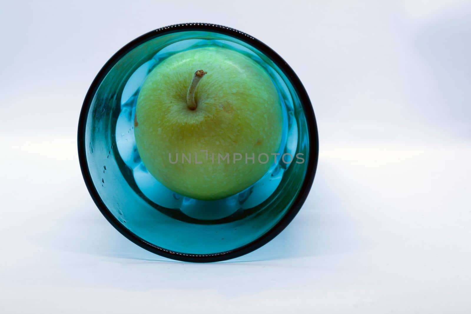 Green apple in a blue glass on a white background close-up.