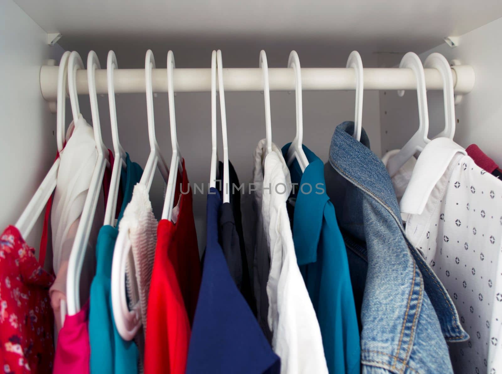 
Clothes on hangers in the closet. Photo of colored clothes on white hangers in the closet.