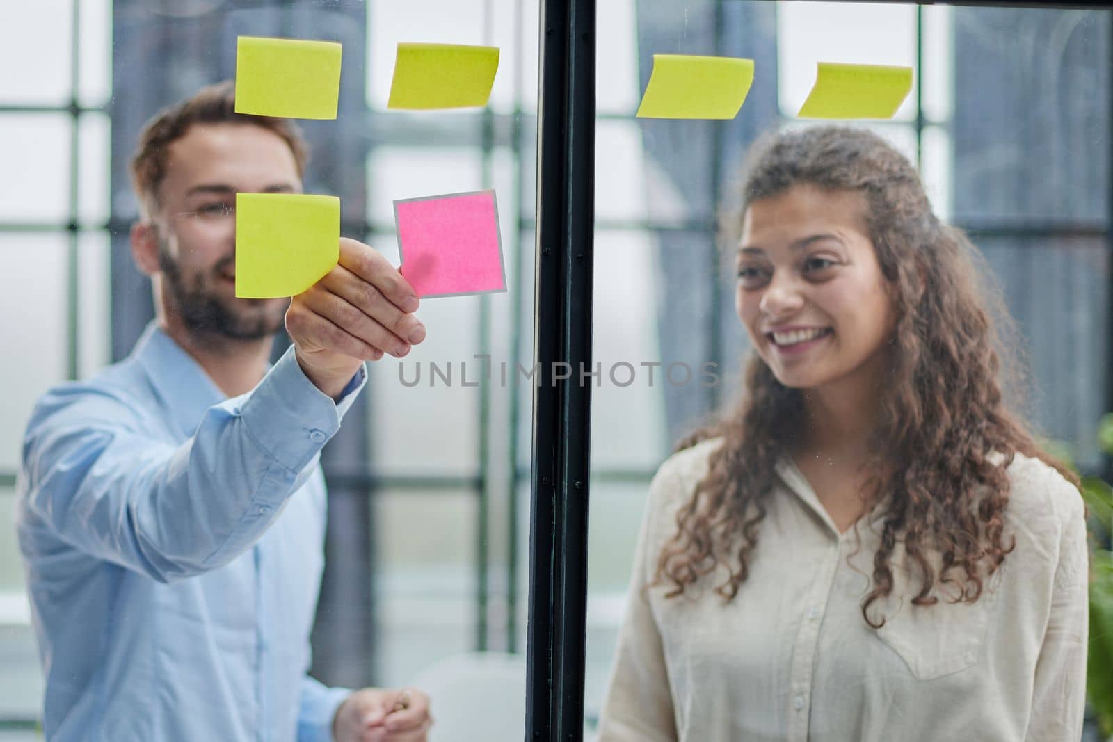 Creative professionals standing and discussing in office behind glass wall with sticky notes