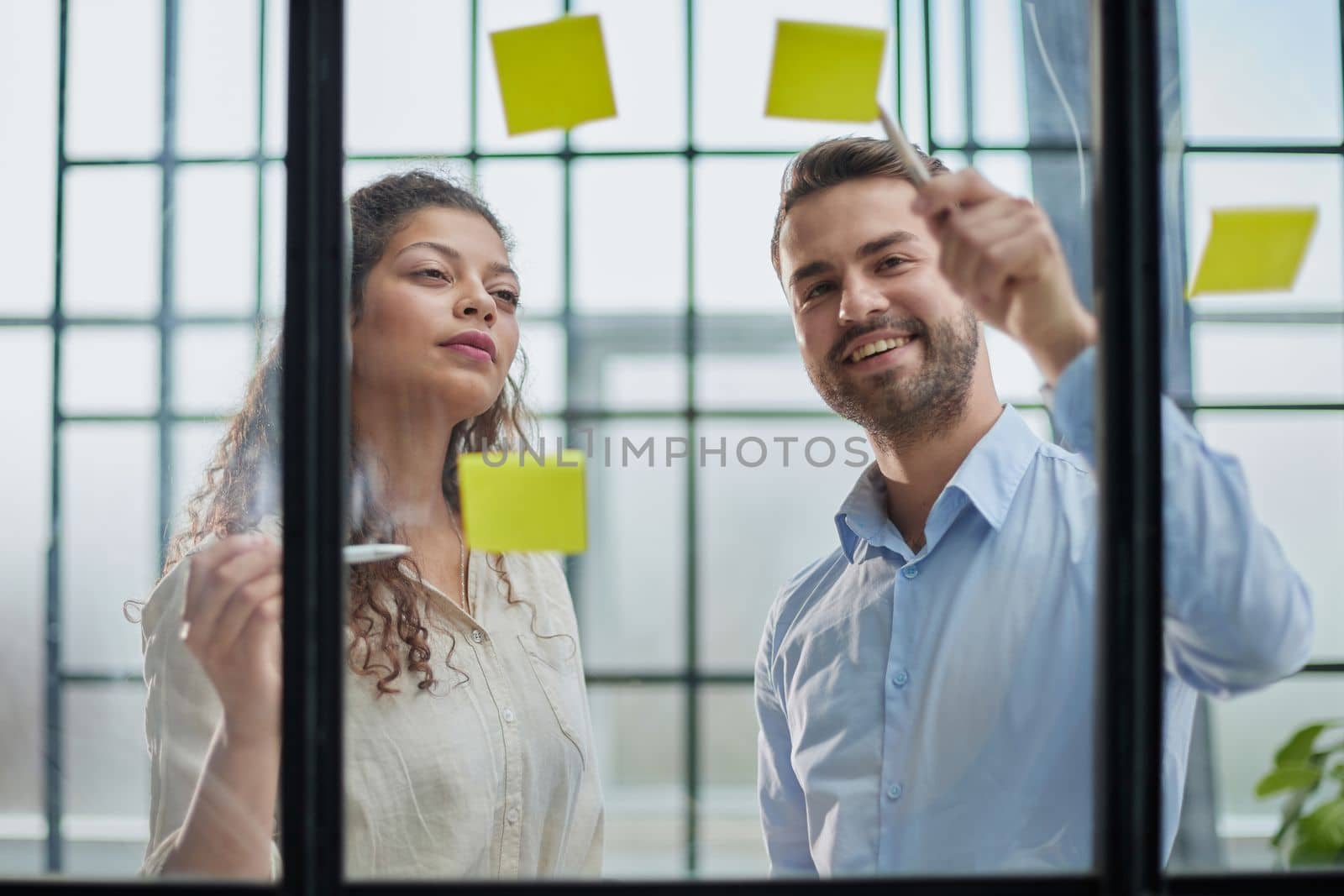 Creative professionals standing and discussing in office behind glass wall with sticky notes