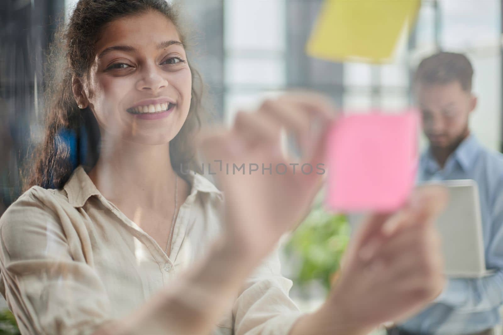 Bringing her vision to life. Shot of a confident businesswoman presenting an idea to her colleague using adhesive notes on a glass wall in the office. by Prosto