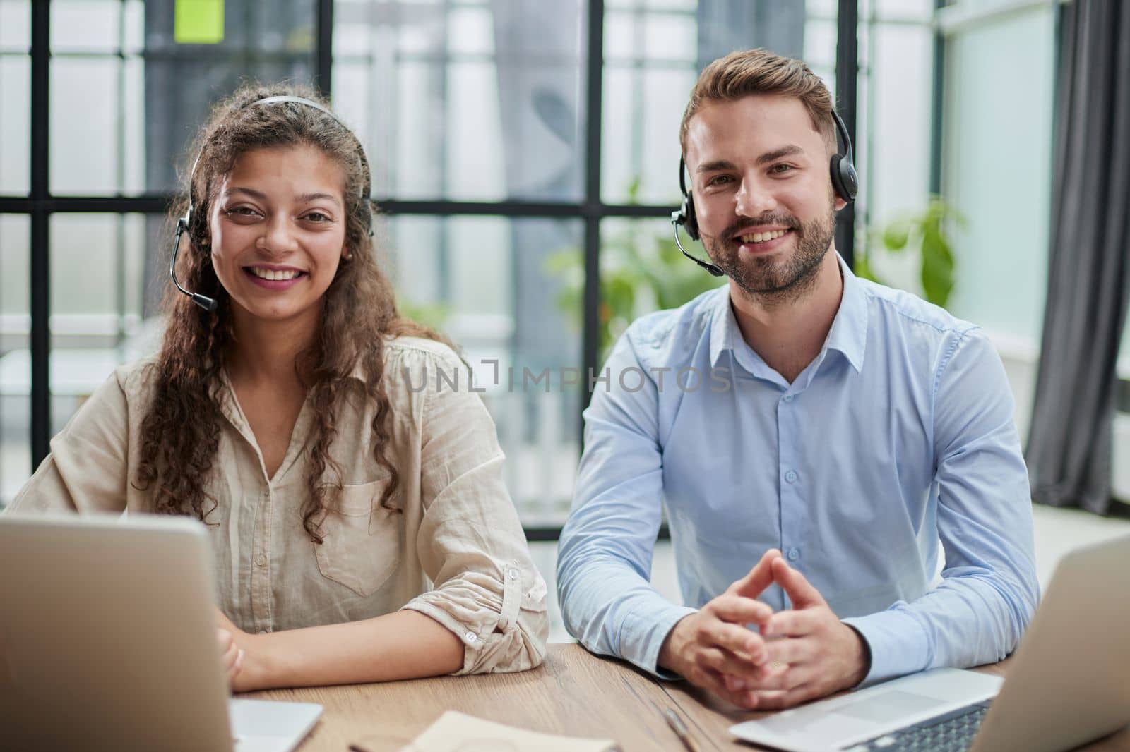 Attractive man and charming woman are sitting at laptops in headphones