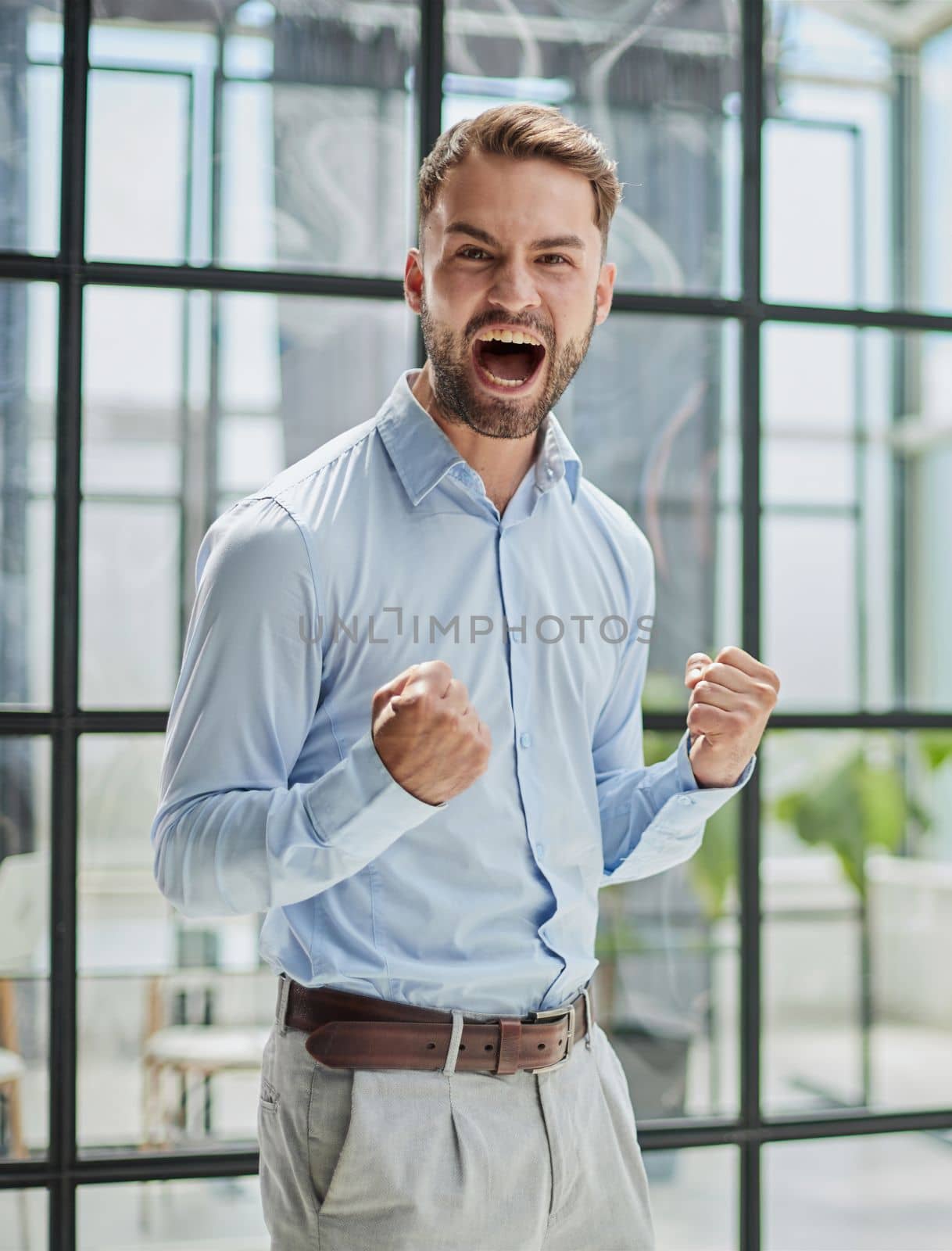 Portrait of a young businessman in a blue shirt shaking his fists celebrating his success in the office