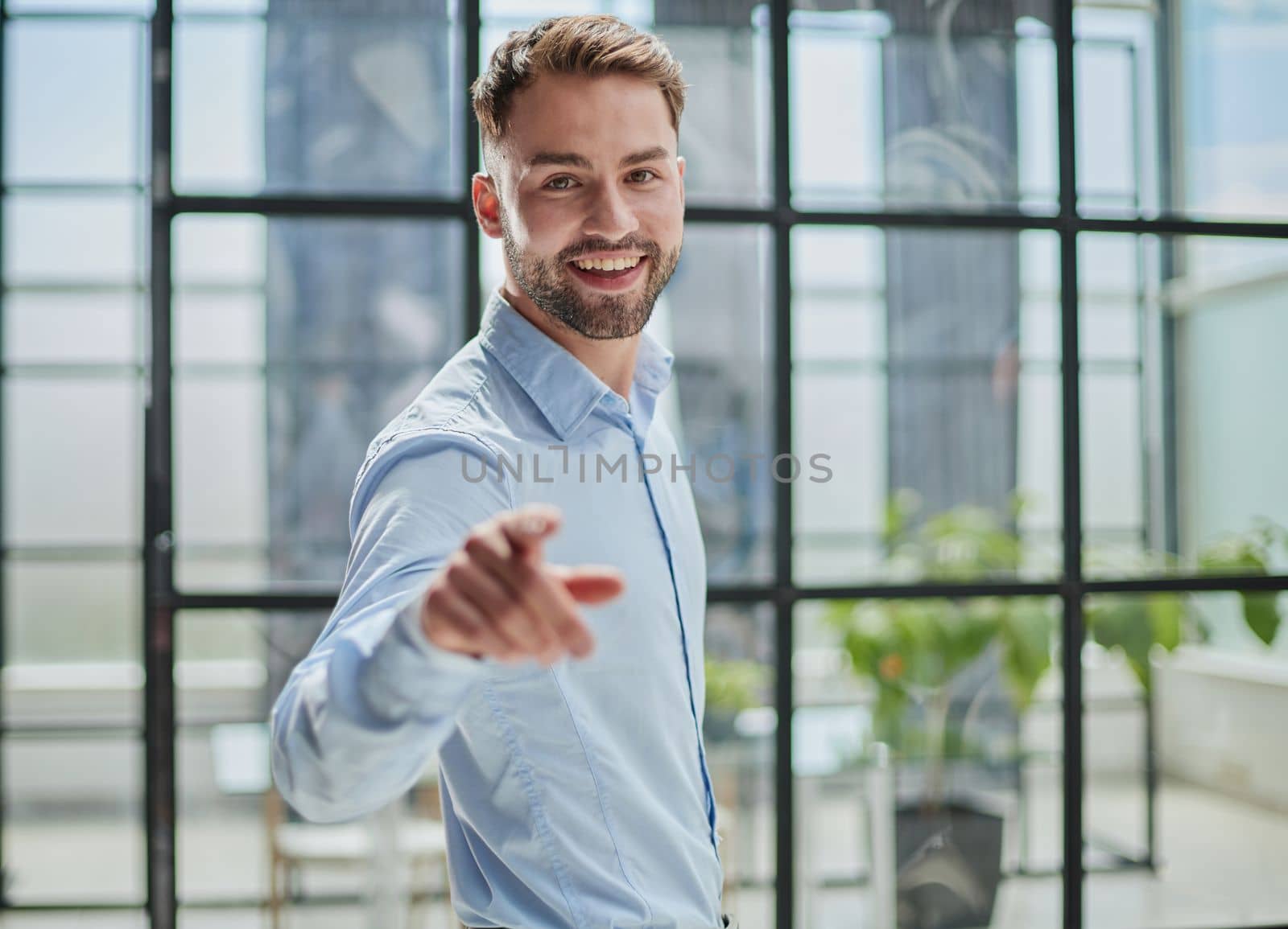 portrait of young businessman in blue shirt pointing finger at camera in office