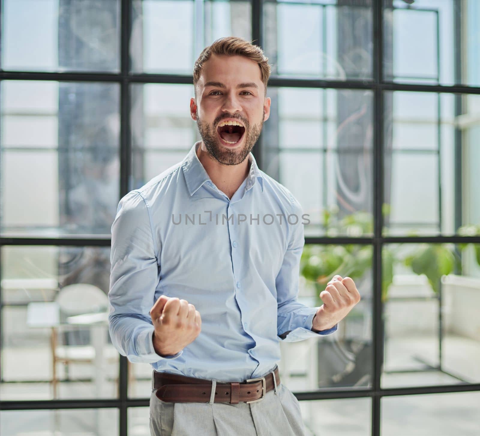 Portrait of a young businessman in a blue shirt shaking his fists celebrating his success in the office