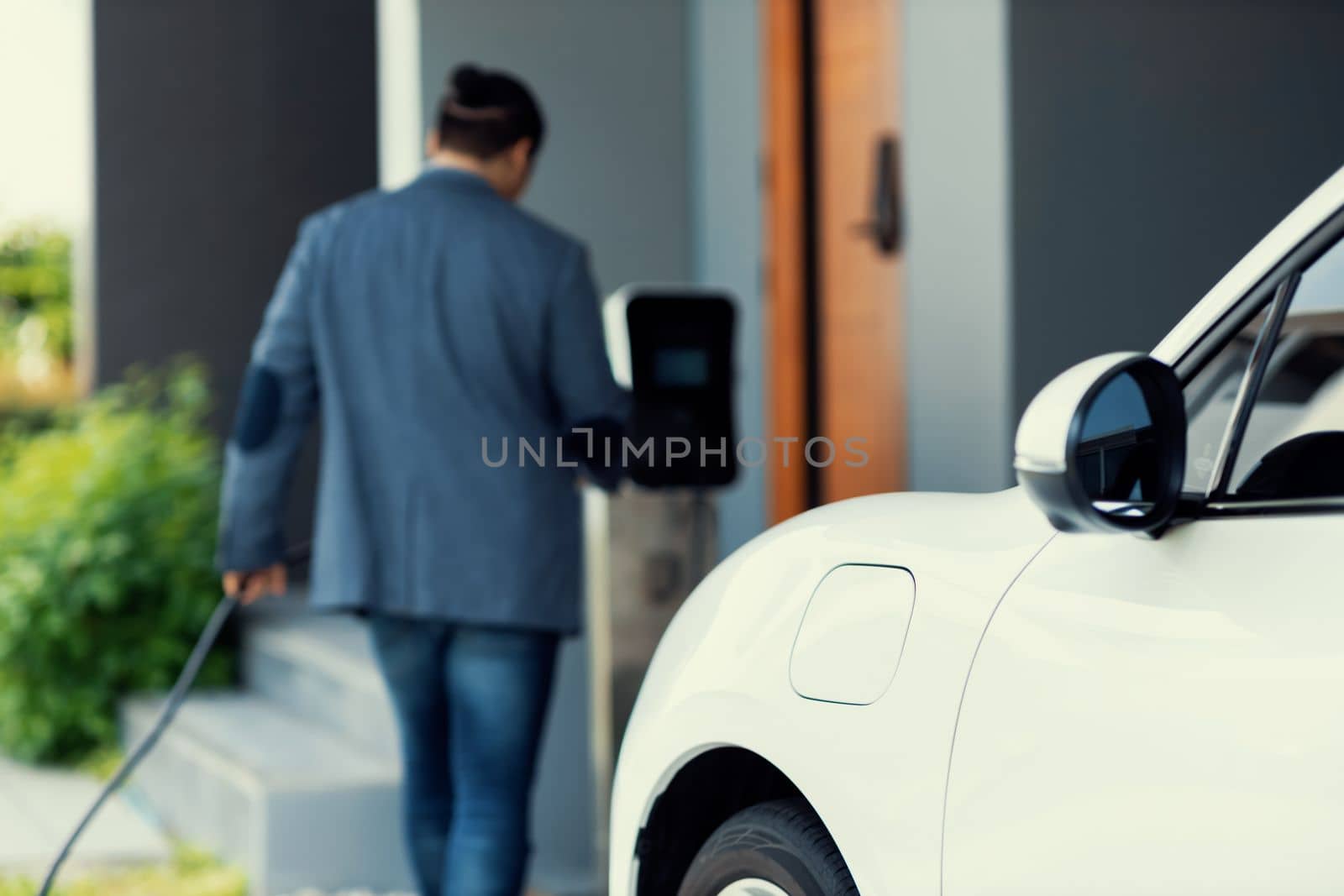 Focus EV charging station at home with blur progressive man in background. by biancoblue