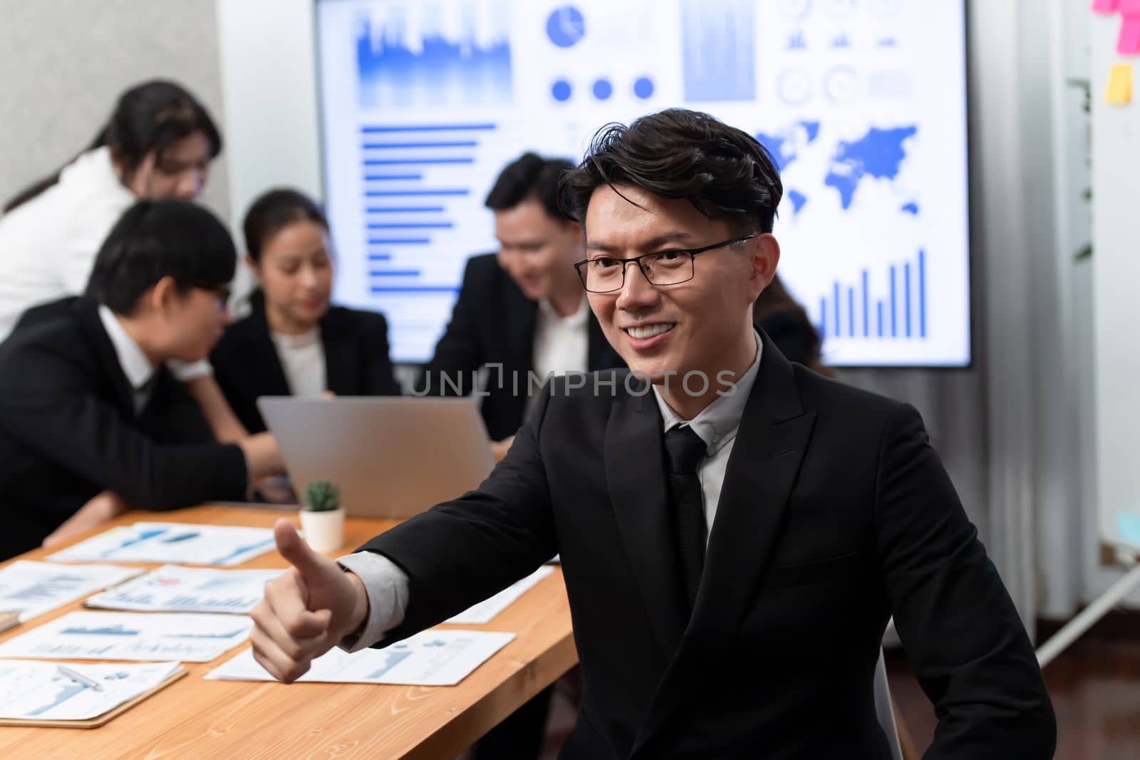 Focus portrait of successful confident male manager or executive in business wear with blurred background of businesspeople, colleagues working with financial report papers in office of harmony.