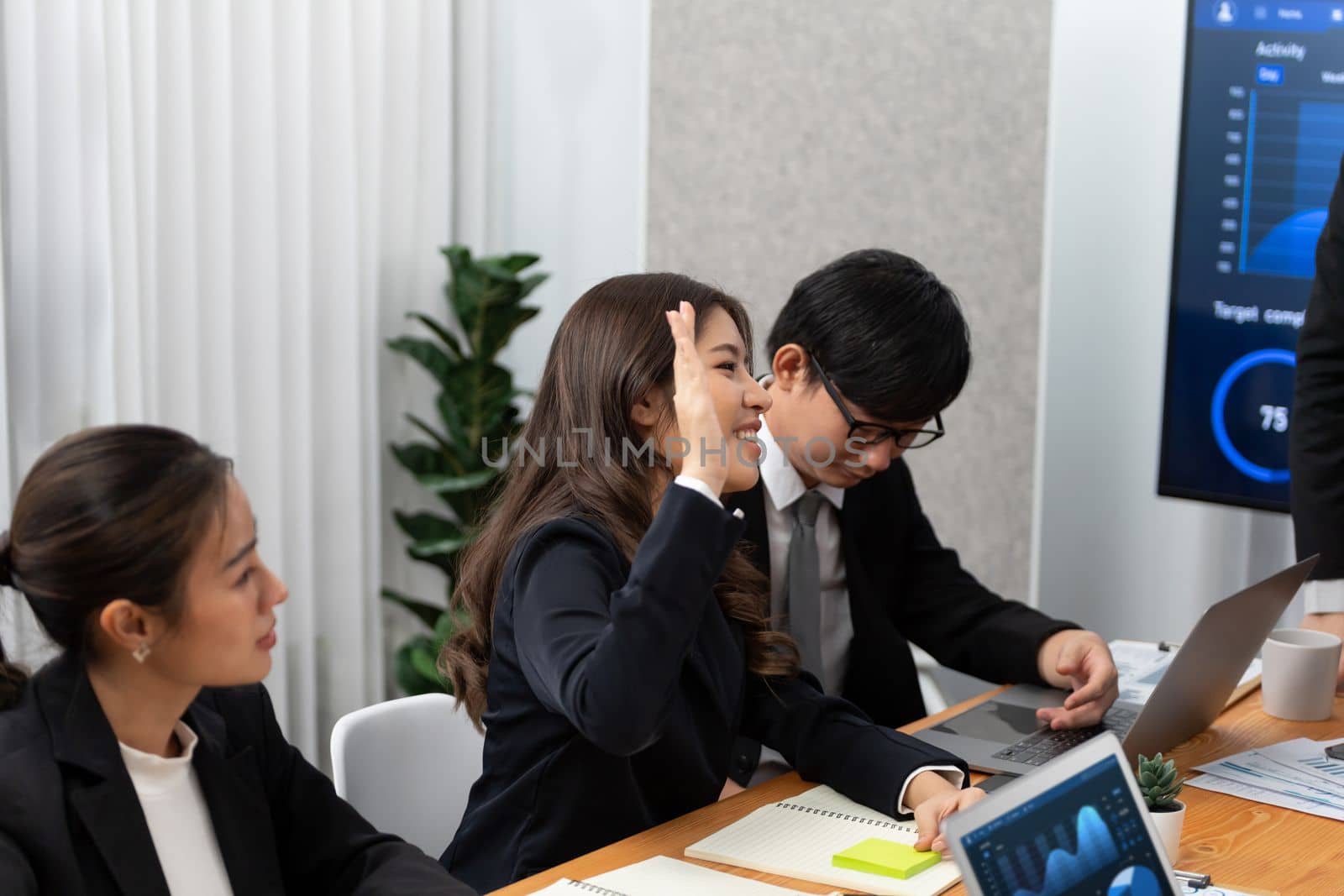 Harmony group businesspeople in meeting room during presentation with dashboard BI financial data displayed on screen, motivated employee raising hand asking question as productive teamwork concept.