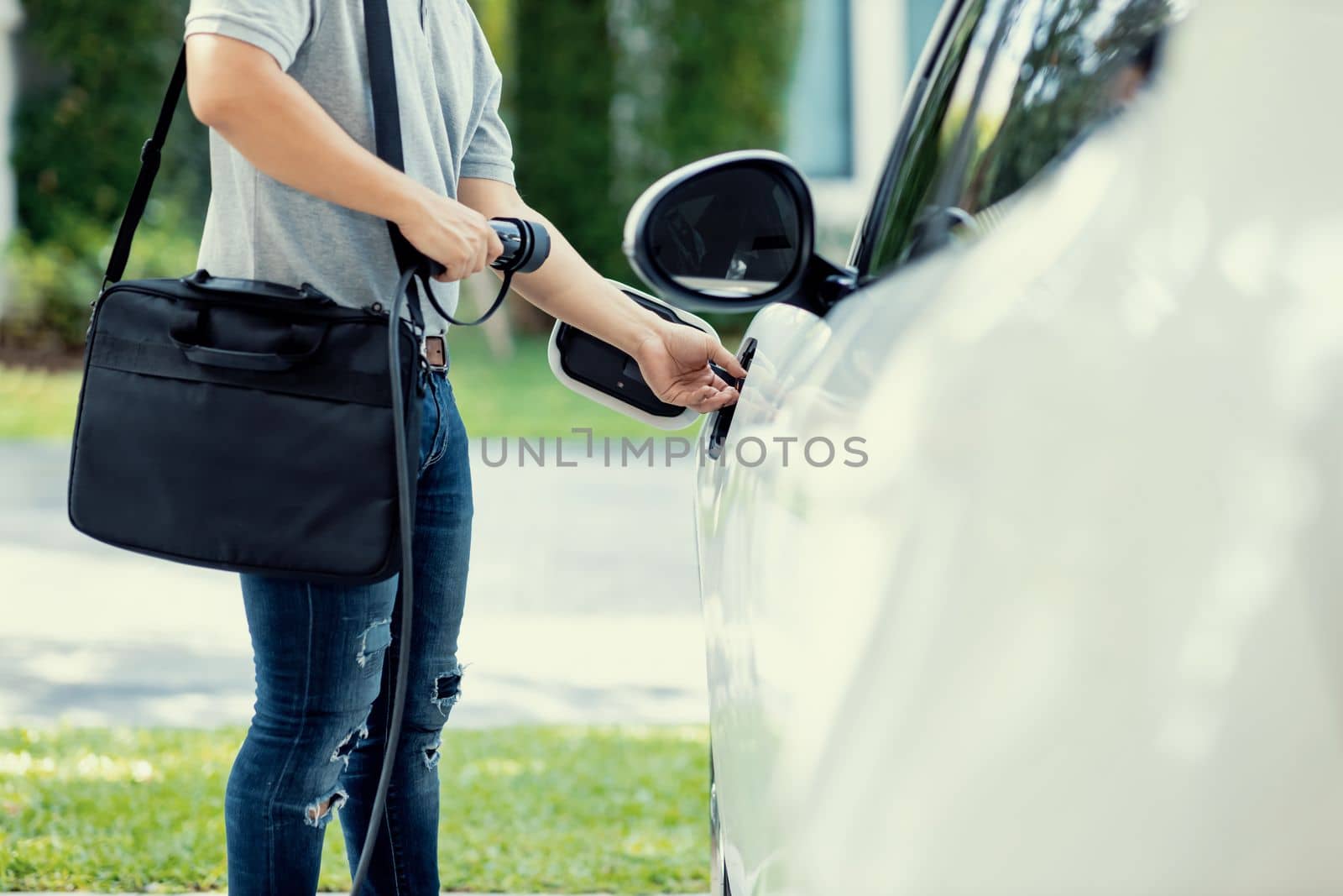 Progressive asian man install cable plug to his electric car with home charging station in the backyard. Concept use of electric vehicles in a progressive lifestyle contributes to clean environment.