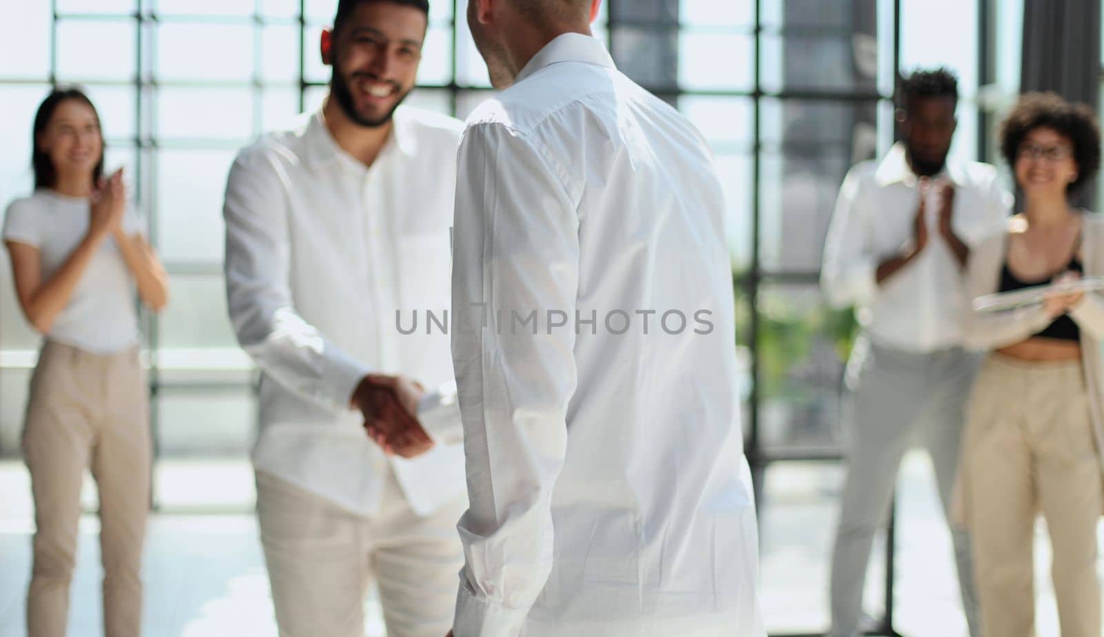 Glad to work with you. Young modern men in smart casual wear shaking hands and smiling while working in the creative office