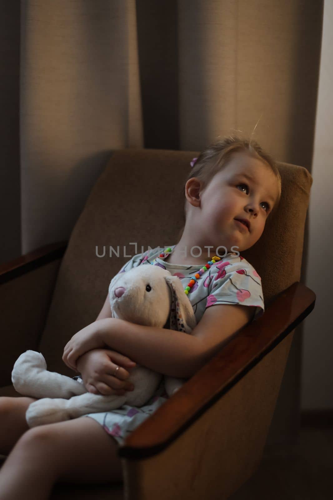 Adorable toddler girl playing indoors with toy sitting in the chair in a cozy room.