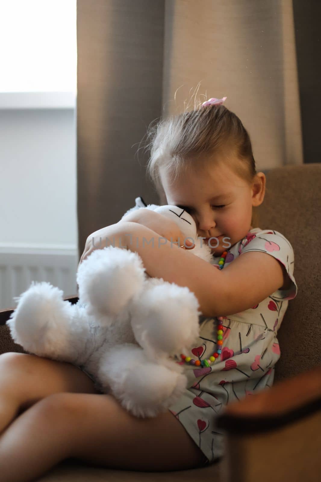 Adorable toddler girl playing indoors with toy sitting in the chair in a cozy room.