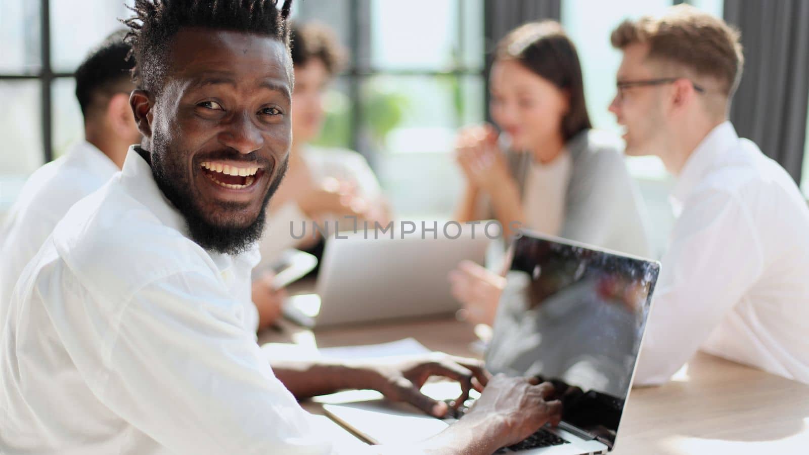 Portrait of smiling African American business man with executives working on laptop in background.