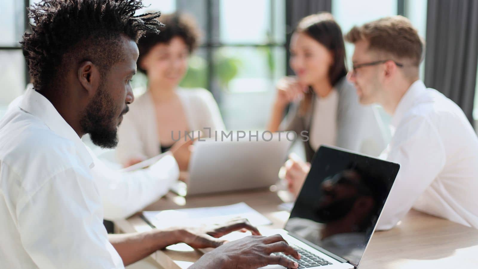 Portrait of smiling African American business man with executives working on laptop in background.