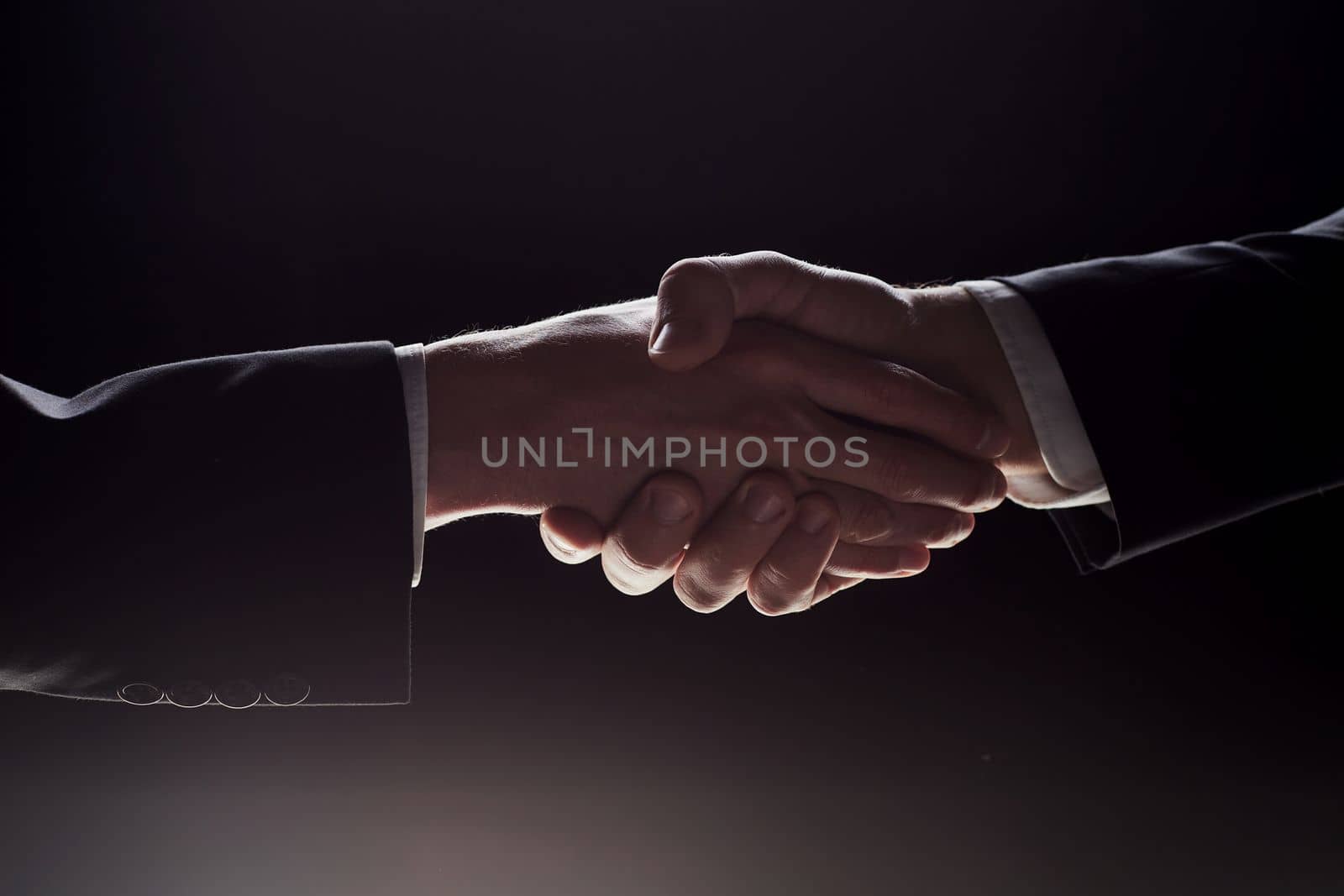 Photo of two men in suits shaking hands on a black background by Prosto