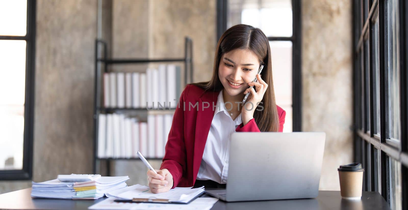 Portrait of a cheerful young business Asian woman using smartphone application in workplace office, concept of Small business employee freelance online sme marketing e-commerce telemarketing...