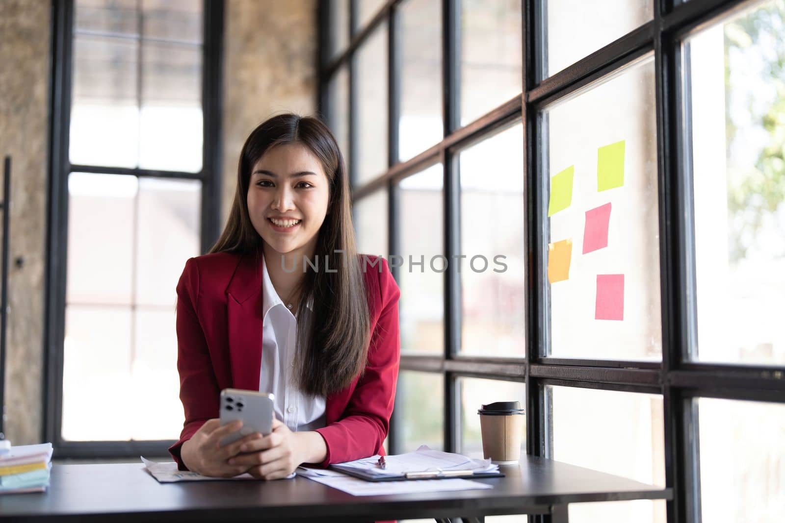 Young smiley attractive, businesswoman using sticky notes in glass wall to writing strategy business plan to development grow to success by wichayada