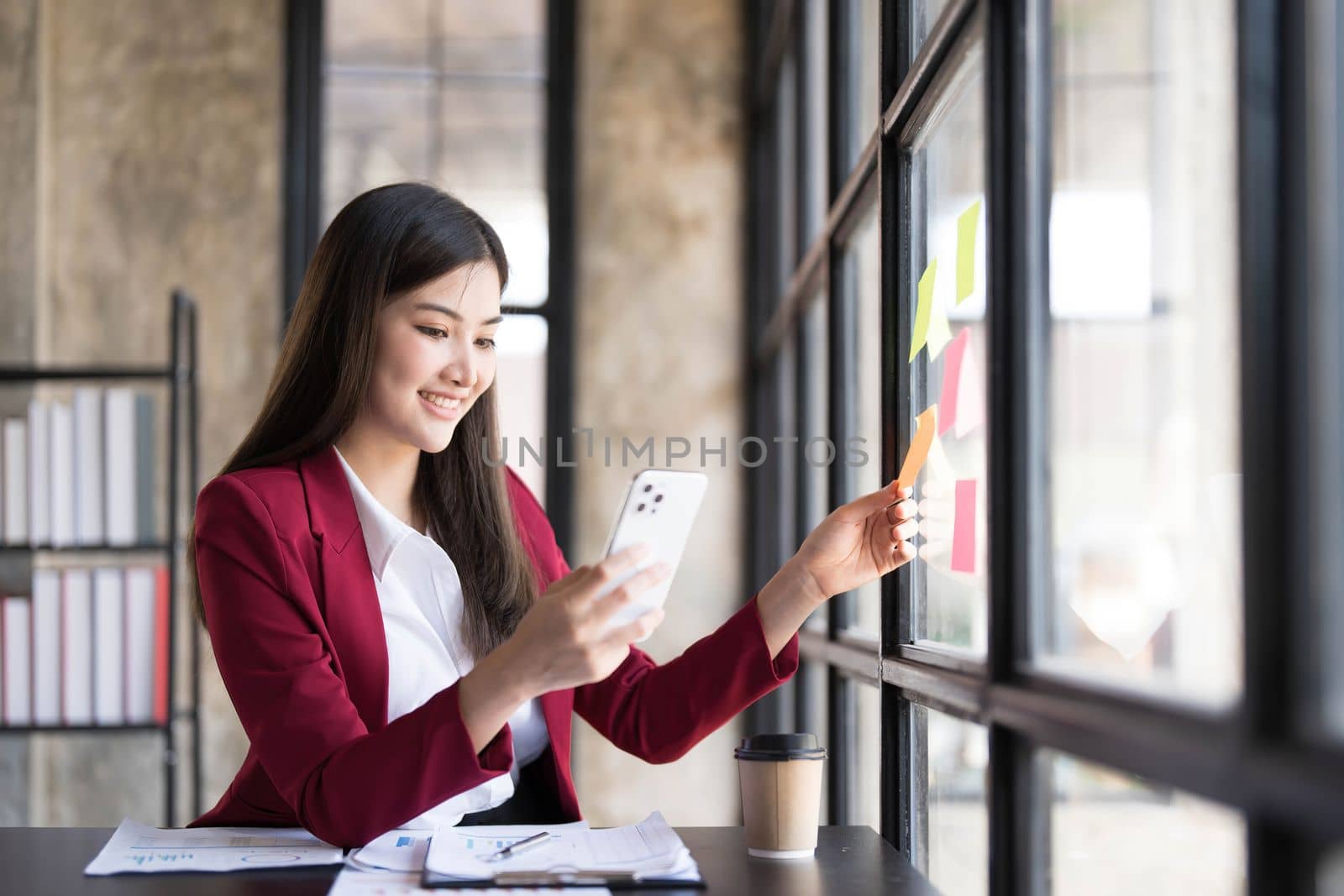 Young smiley attractive, businesswoman using sticky notes in glass wall to writing strategy business plan to development grow to success..