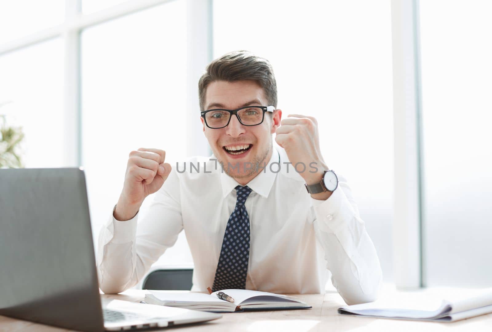 Happy young businessman raising hands in front of laptop