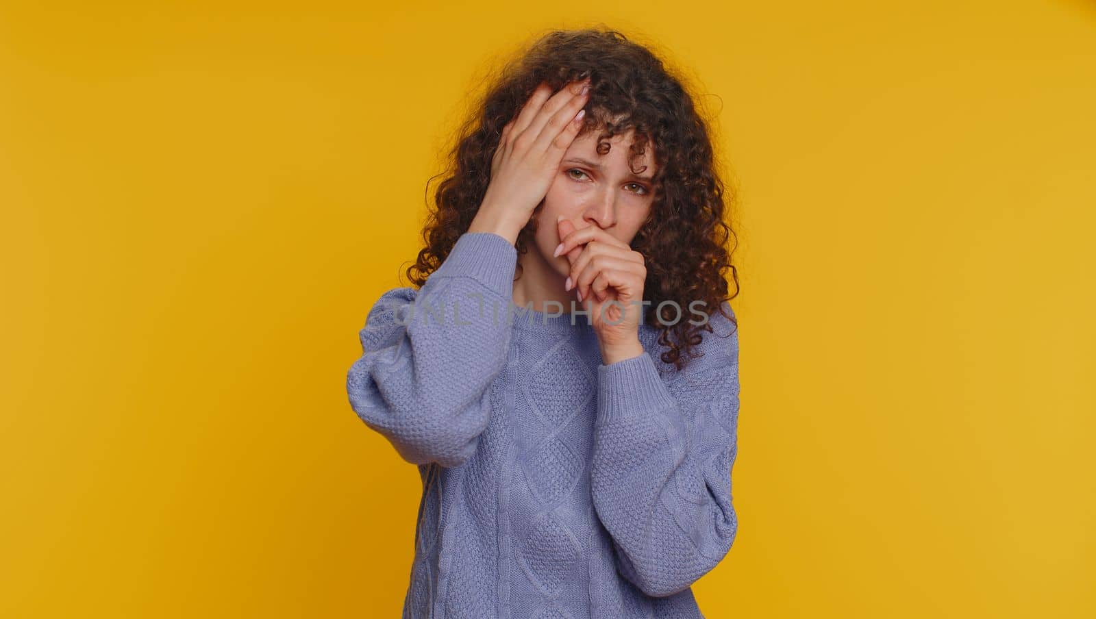 Unhealthy curly haired woman coughing covering mouth with hand, feeling sick, allergy, viral infection symptoms, coronavirus pandemic. Young adult teen girl isolated alone on yellow studio background