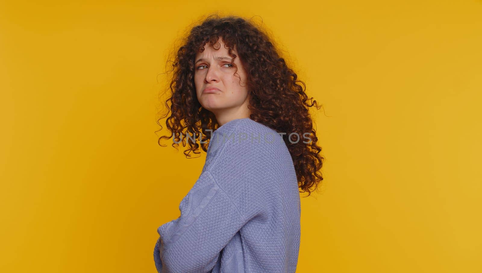 Offended sad curly haired woman having misunderstanding, frustrated after quarrel, ignores and does not want to communicate talk, depression. Young teen girl isolated alone on yellow studio background
