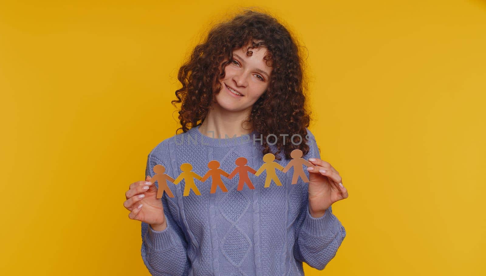 Woman showing multiracial different skin color human shape cut out of paper, concept of teamwork, partnership, community, unity, people support love, against racism. Young girl on yellow background