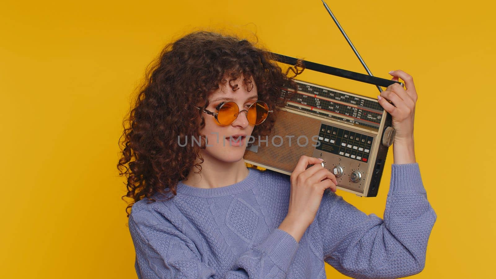 Curly haired woman using retro tape record player to listen music, disco dancing of favorite track, having fun, entertaining, fan of vintage technologies. Young teen girl isolated on yellow background