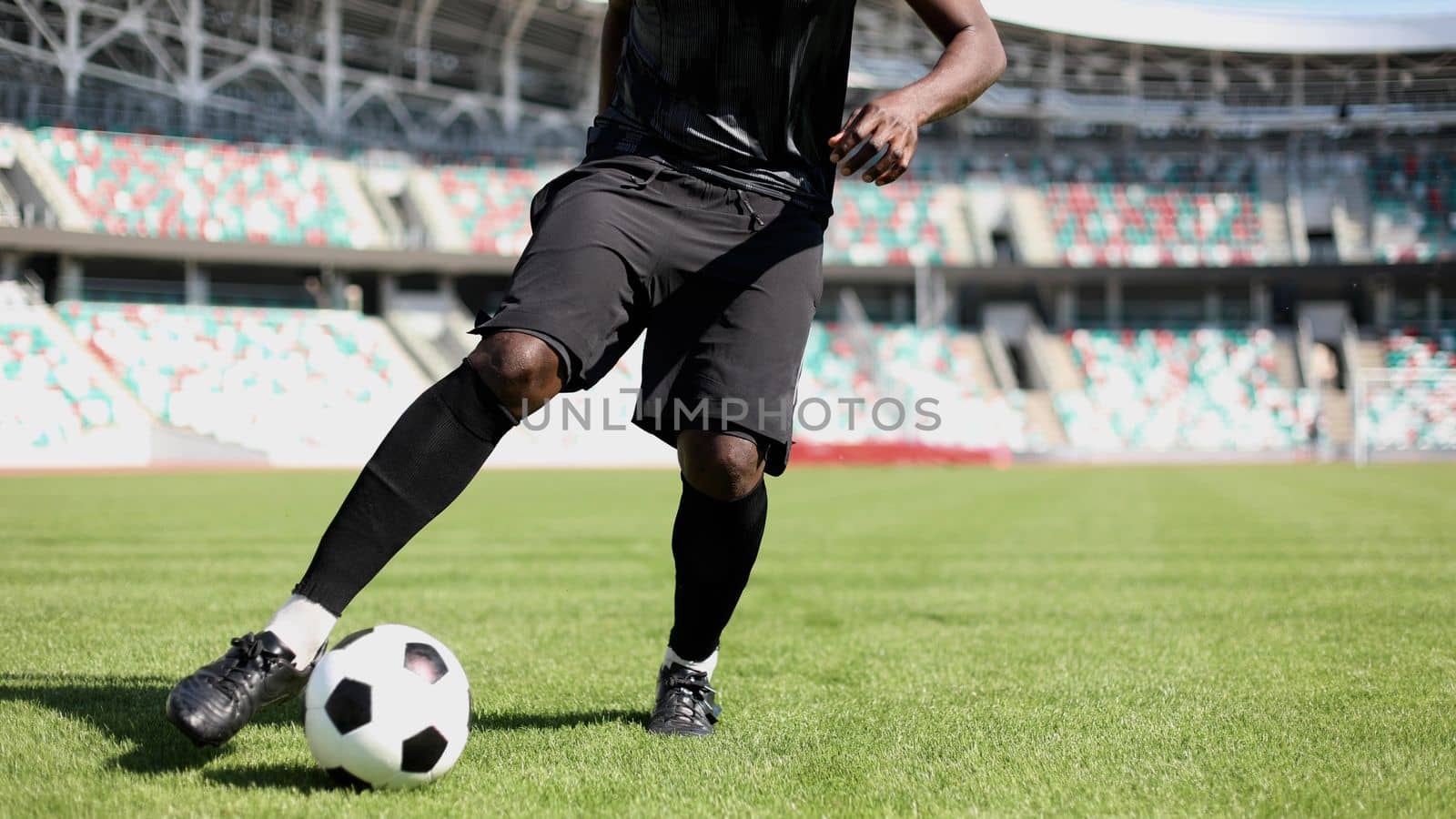 African American man playing football on the stadium field. A man runs with a soccer ball across the field. by Prosto