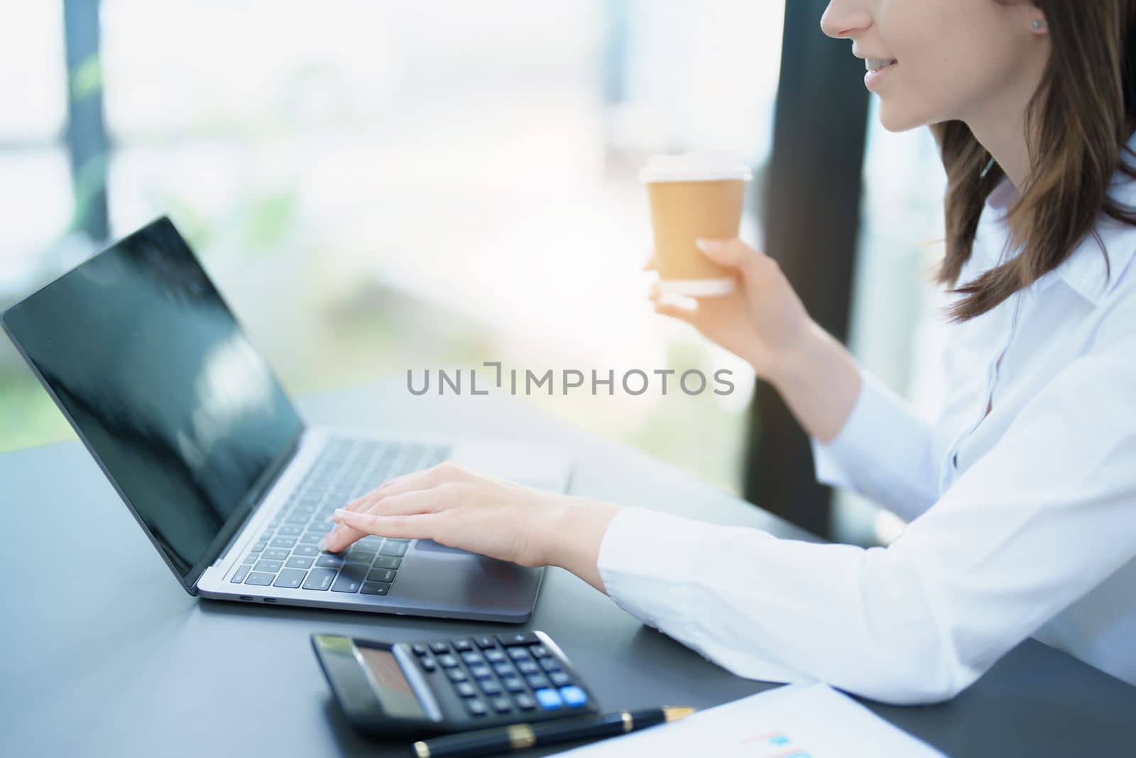 Portrait of a business woman using laptop computer and drinking coffee. by Manastrong